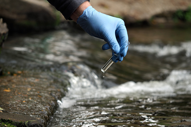 Person collecting water sample with a glass beaker